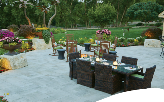 Outdoor patio dining area with wicker chairs, tables, flowers, and garden landscaping