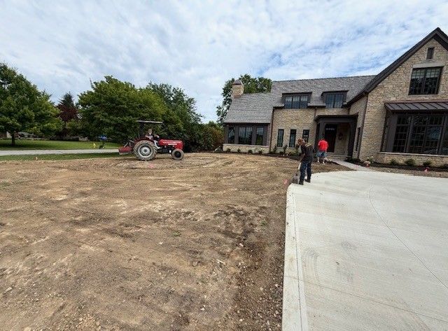 Construction site with a red tractor, dirt lot, and two people near a stone building