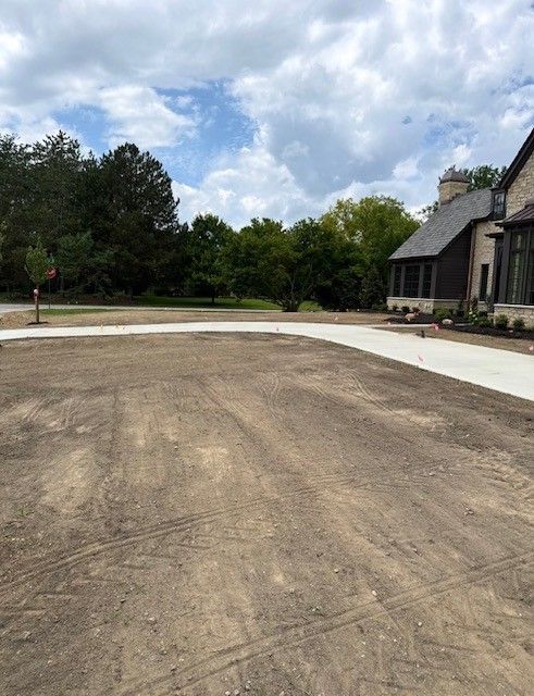 Partially paved driveway beside a house, with trees and a cloudy sky in the background