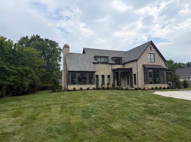 Large modern stone house with a steep roof and wide lawn under a cloudy sky
