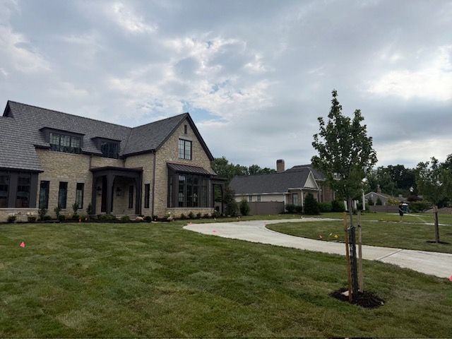 Large modern house with stone facade, curved driveway, and grassy lawn under cloudy sky