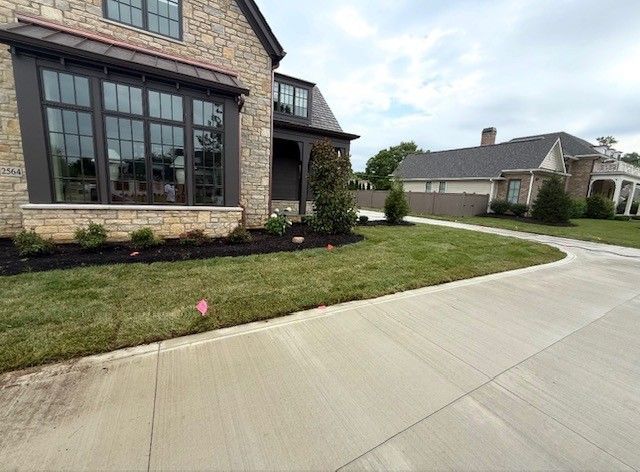 Brick house with large windows, landscaped lawn, and wide concrete driveway in a suburban neighborhood