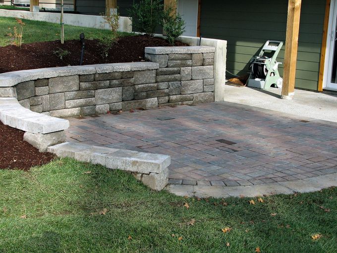 Stone patio with curved retaining wall beside a grassy yard and house garage.
