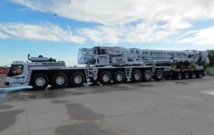 Large white crane on wheels parked on concrete, under a blue sky.