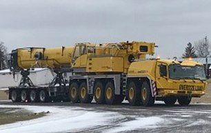 Yellow crane on a trailer, labeled "OVERSIZE LOAD", parked on snow.