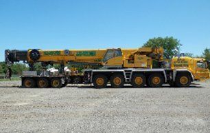 Yellow crane on a gravel lot, boom extended, with trailer attached.
