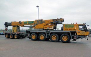 Yellow mobile crane on pavement with trailer.