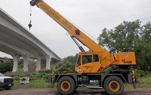 Yellow crane lifting near a highway overpass.
