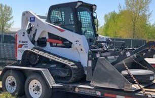White and gray Bobcat skid-steer loader with tracks on a trailer.