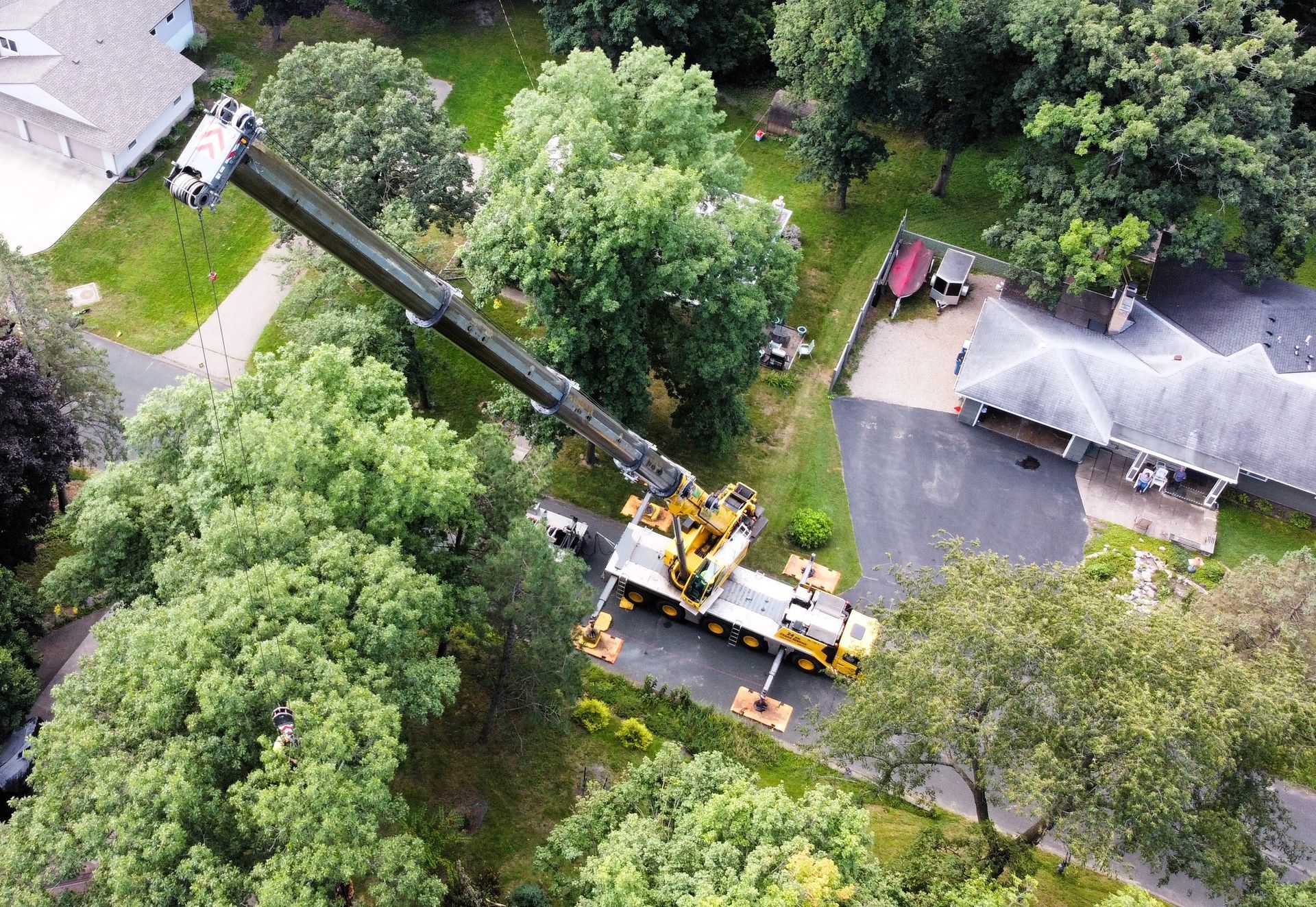 Yellow crane extending over trees in a residential area, parked near a house.