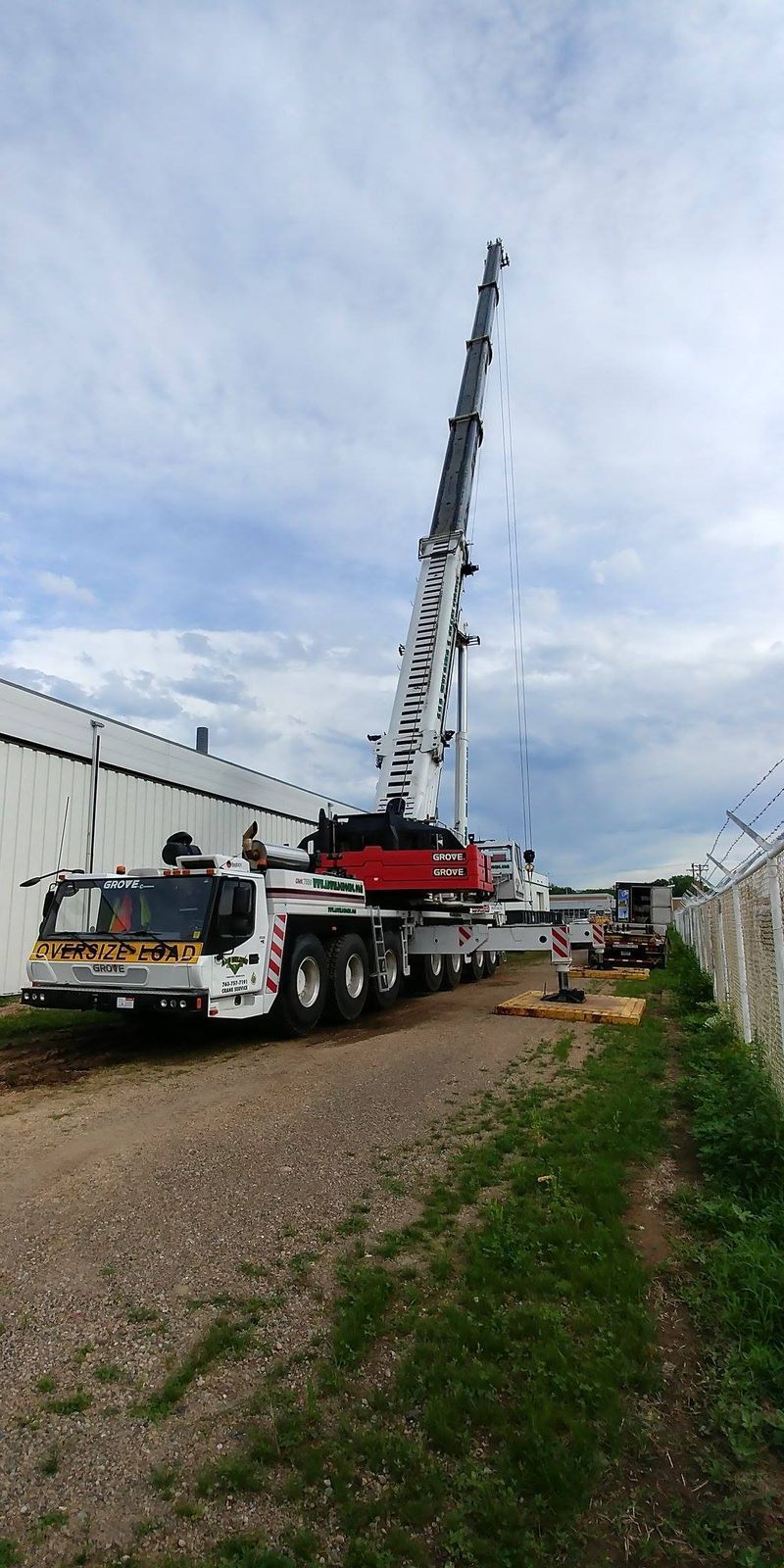 A large white and red crane with its boom extended, parked on a gravel path next to a building.