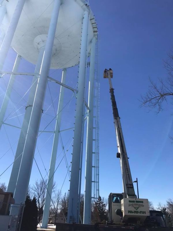 A boom lift next to a tall, light-blue water tower; blue sky, sunny day.