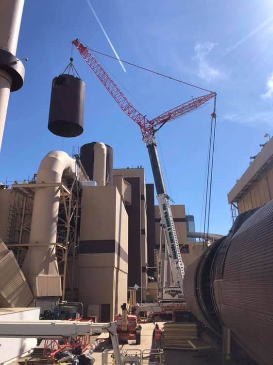 A crane lifting a cylindrical object over an industrial building under a blue sky.
