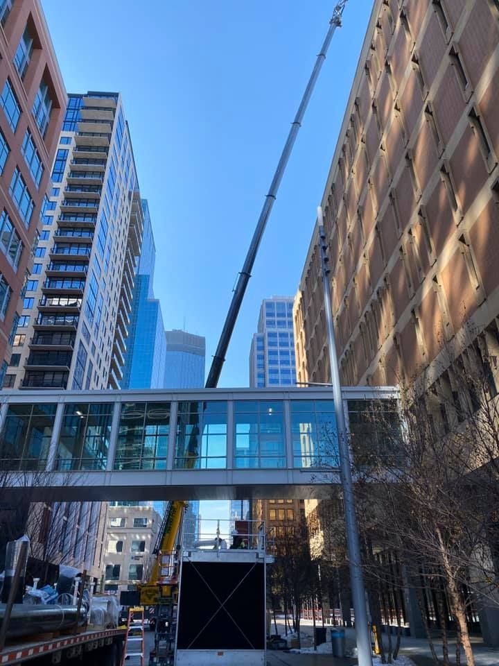 A crane near a skyway between buildings in an urban setting. Bright sky.