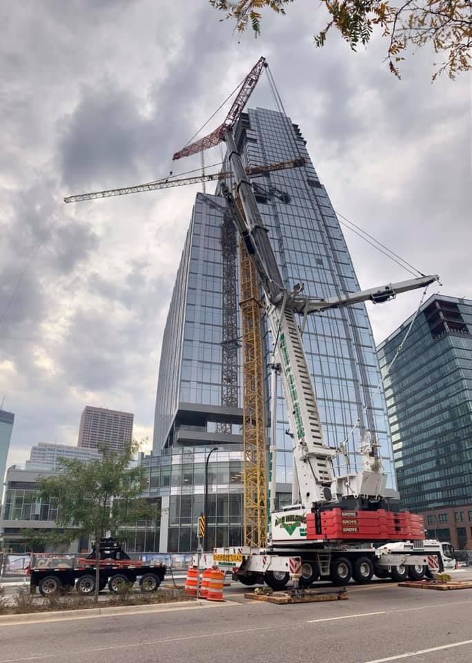 A large crane next to a glass skyscraper under construction in an urban setting, cloudy sky overhead.