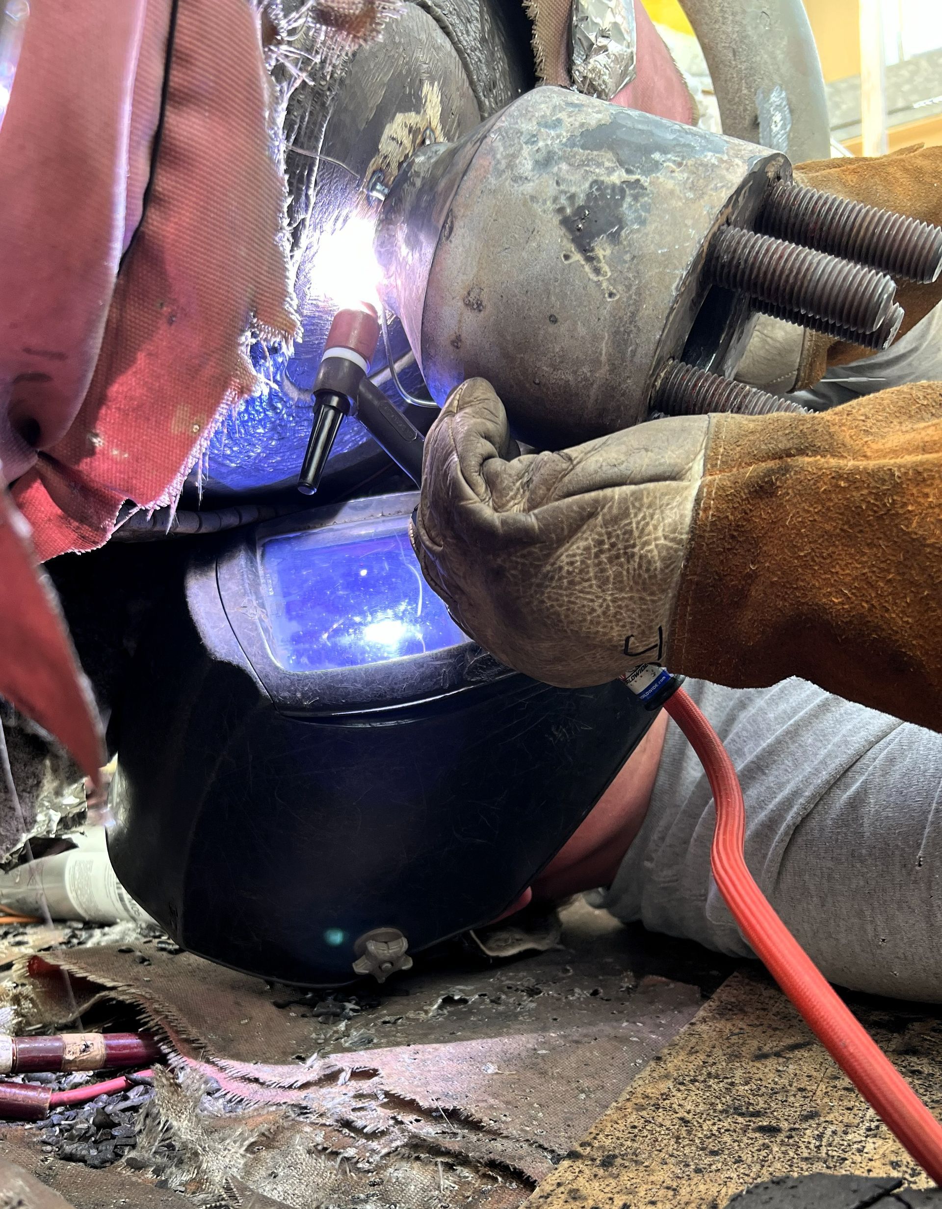 Welder wearing a helmet, welding metal with sparks, wearing protective gloves.