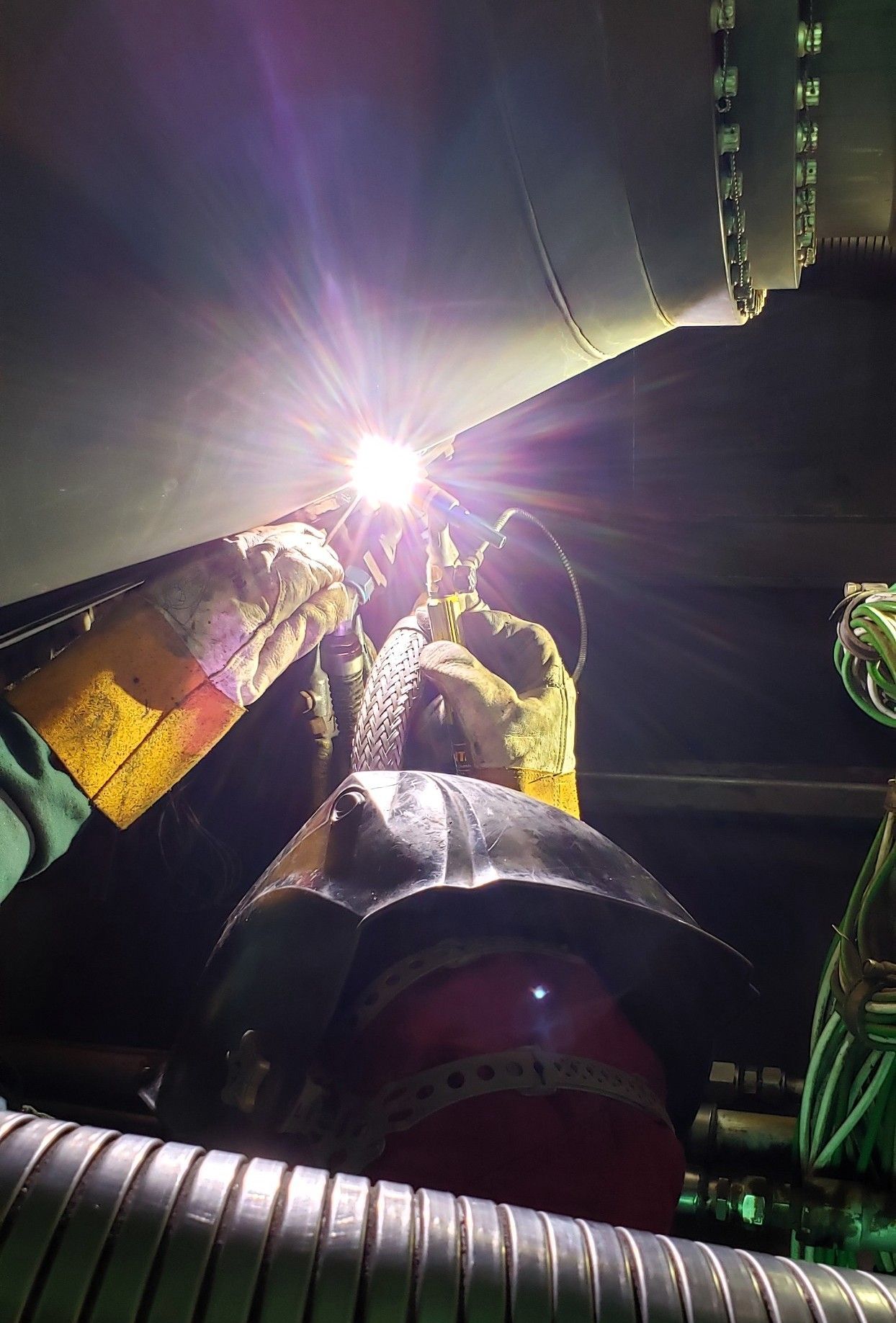 Welder in protective gear welding inside a large metal structure, bright light emanating from the welding torch.