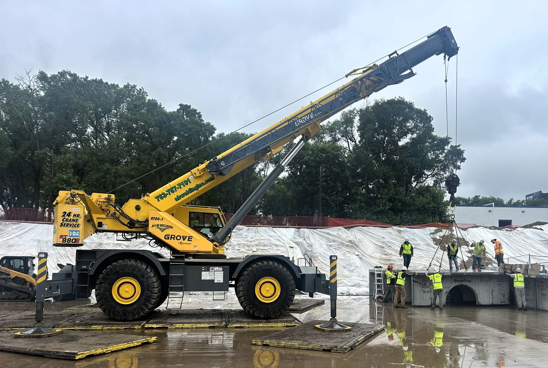Yellow crane lifting concrete structure at construction site. Workers stand nearby.