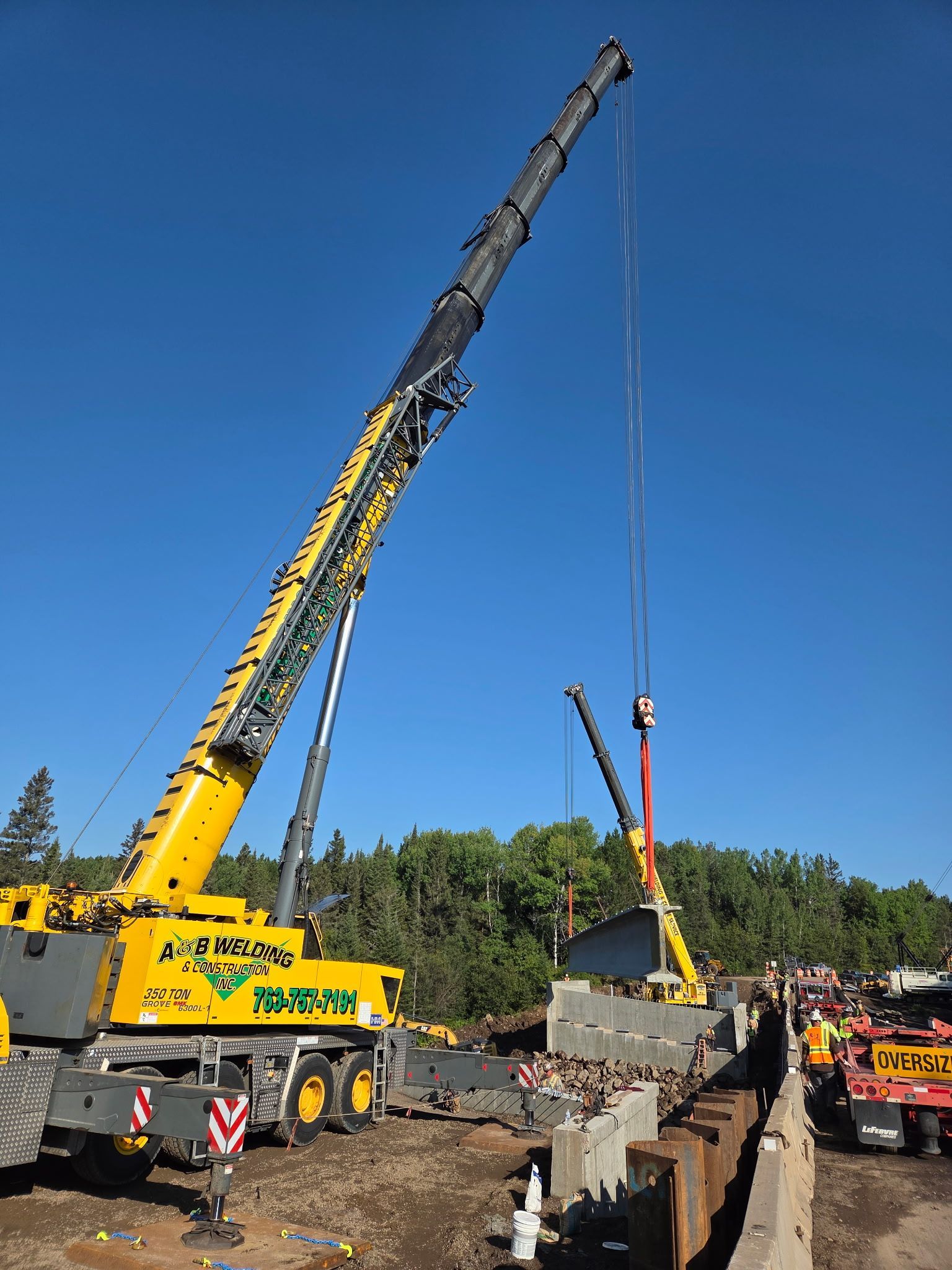 Large yellow crane lifting concrete structure on a construction site; clear blue sky.