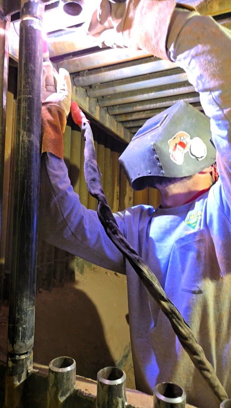 Welder in protective gear welding a metal pipe indoors.