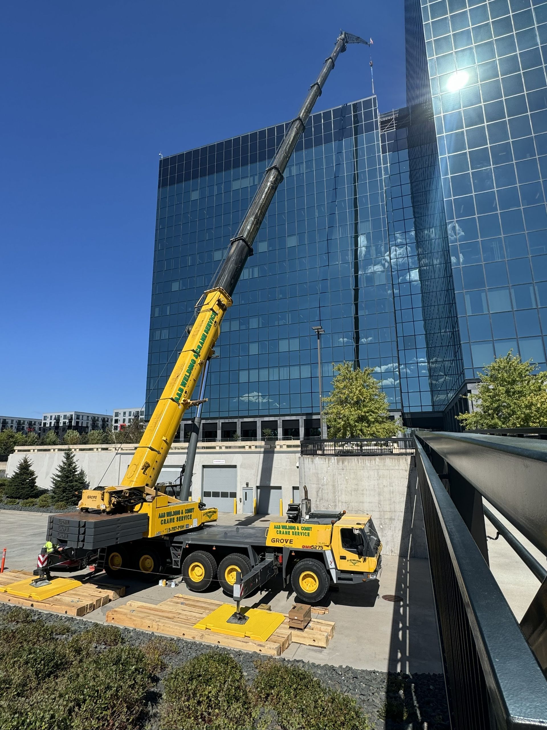 Yellow crane lifting near a blue glass building on a sunny day.