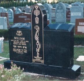 Black granite Jewish tombstone with Hebrew and English inscriptions, menorah, and Star of David in a cemetery.