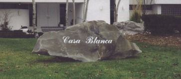A large rock on a grassy lawn with the words
