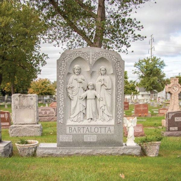 Gravestone with carved figures of a family. Cemetery setting with other headstones.
