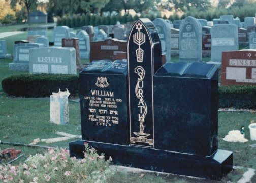 Black granite gravestone with gold Hebrew text and Jewish symbols in a cemetery.