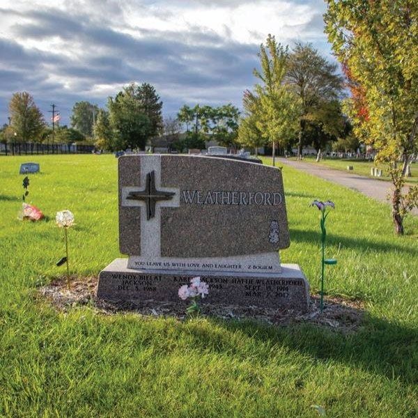 Headstone with cross in a grassy cemetery on a cloudy day.