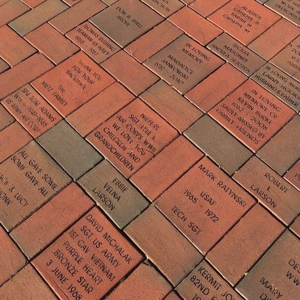 Close-up of engraved bricks in varying shades of red and brown, likely a memorial, with names and dates.