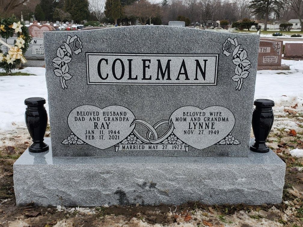Gray headstone with Coleman surname, heart-shaped inscriptions, dates, and two black vases in snowy cemetery.