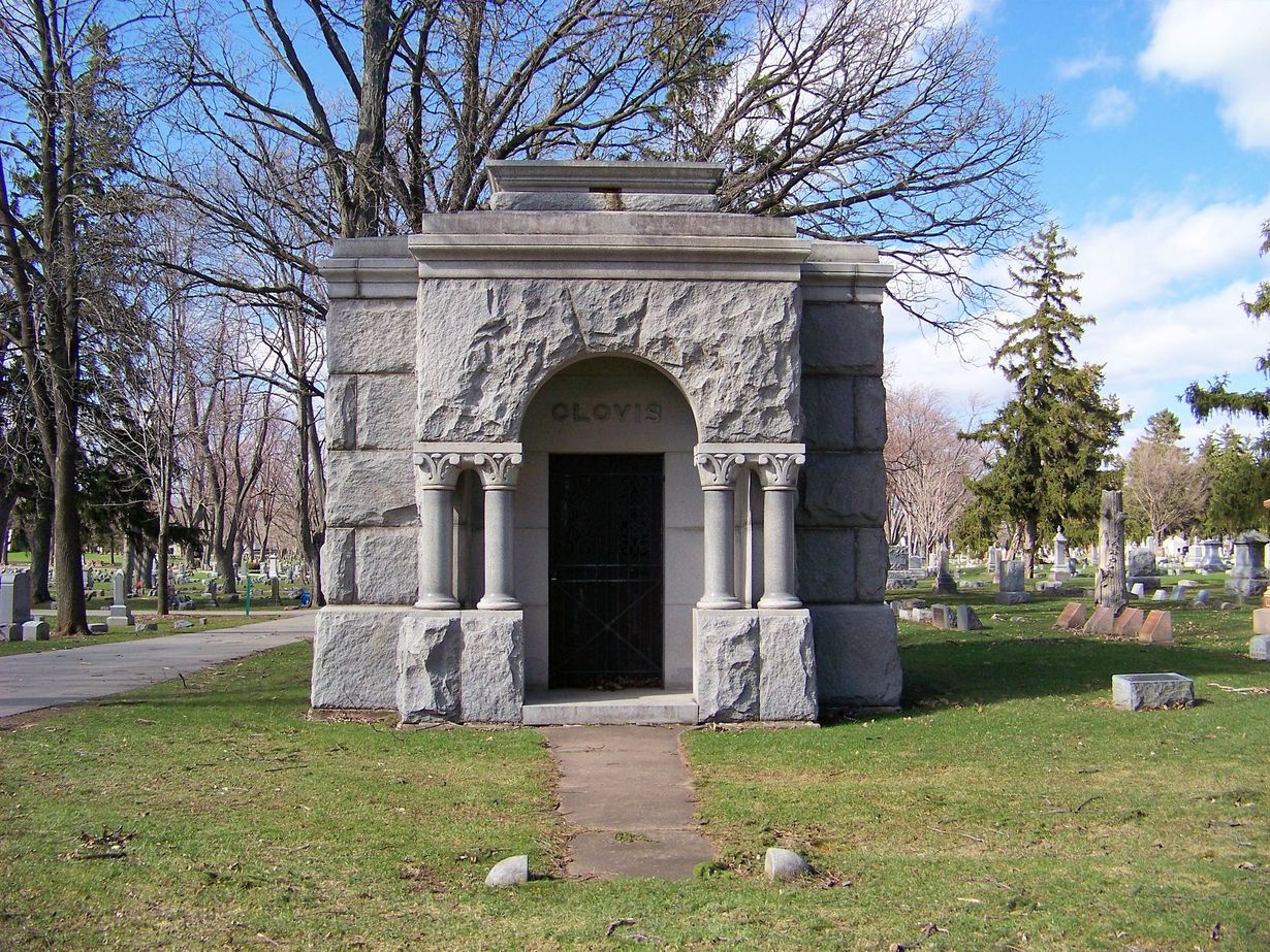 Stone mausoleum in a cemetery with a blue sky.