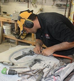 Man carving stone with tools, wearing safety gear in a workshop.