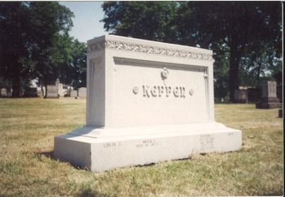 White stone tombstone in a grassy cemetery, with the name