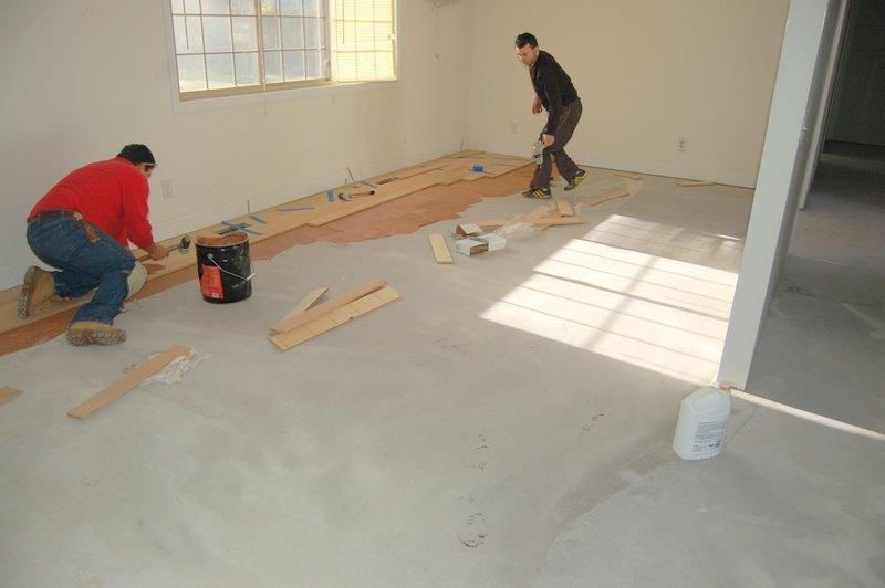 Two men are working on a wooden floor in a room.