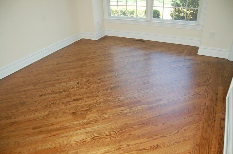 An empty room with hardwood floors and two windows.
