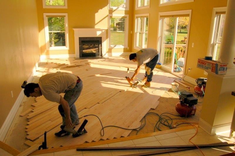 Two men are working on a wooden floor in a living room