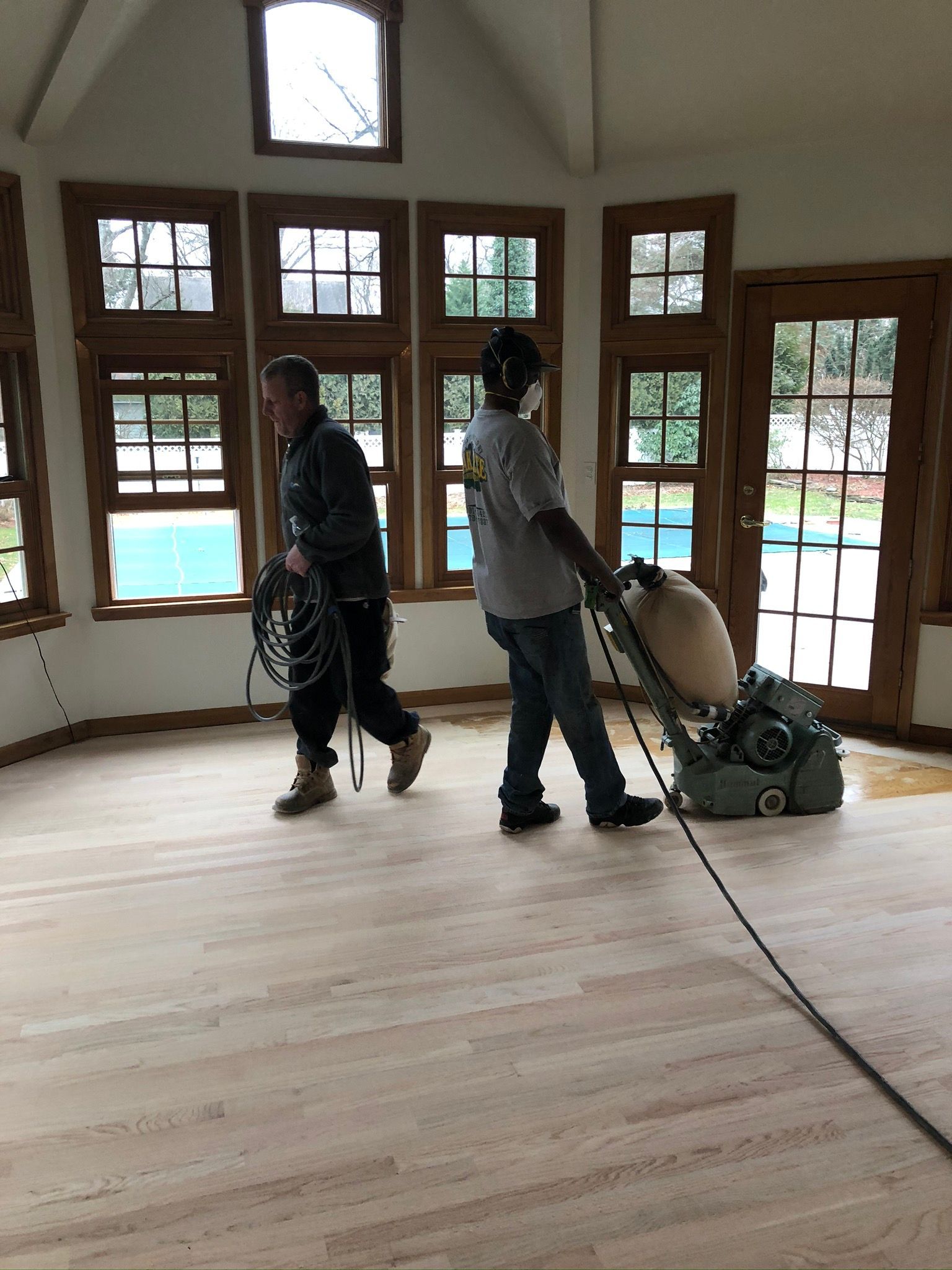 Two men are sanding a wooden floor in a room.