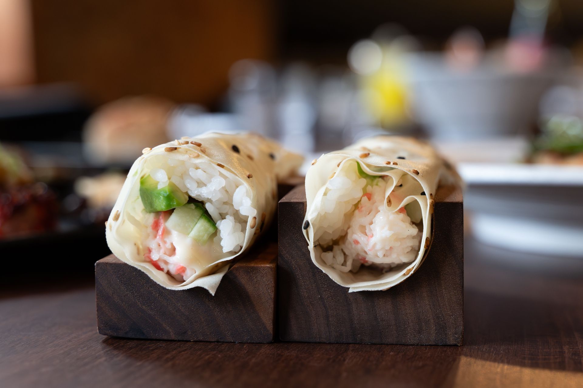 Two sushi rolls on a wooden stand with a blurred restaurant background