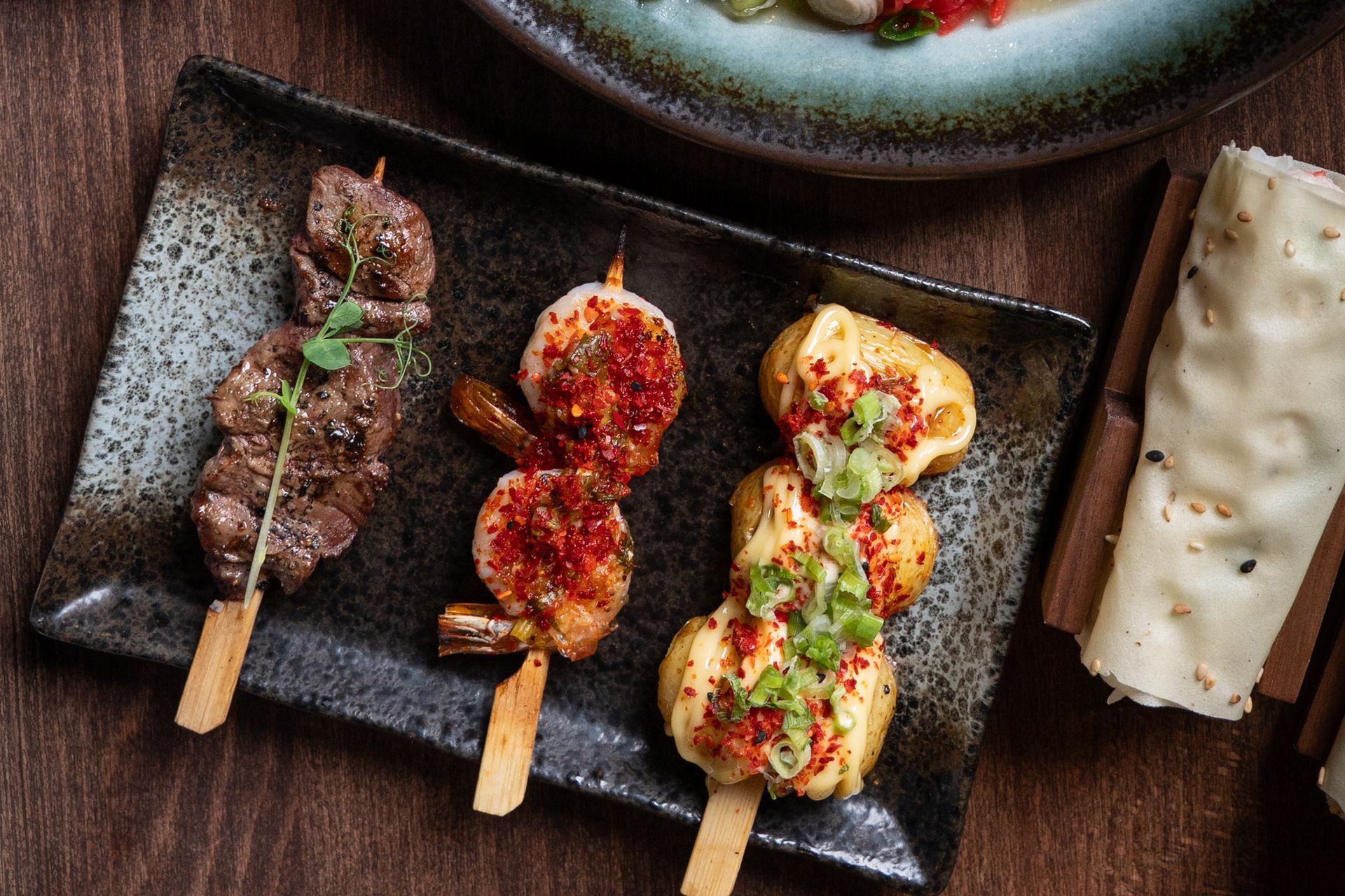 Grilled meat and green onion on skewers on a white platter on a gray table
