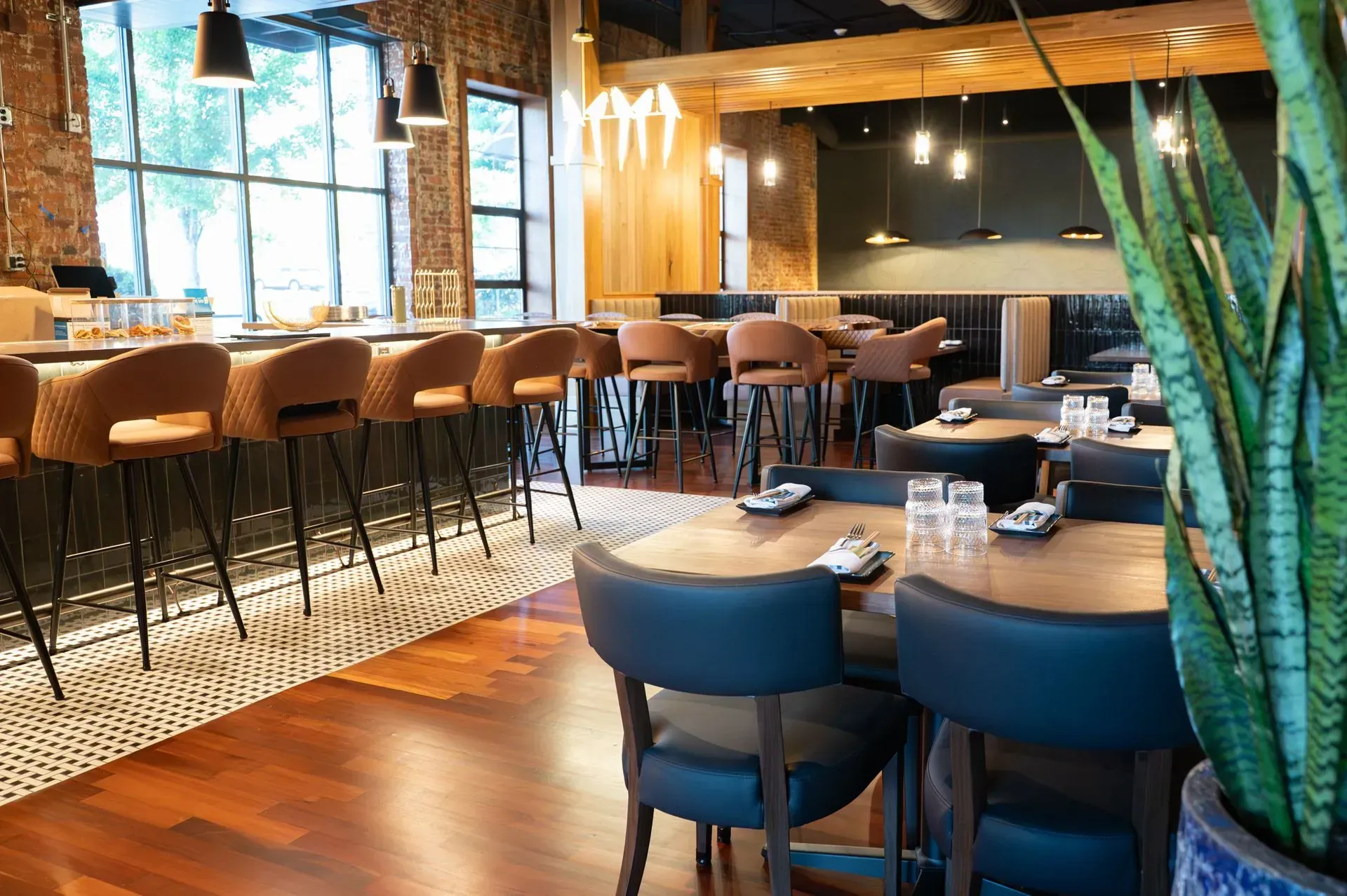 Modern restaurant interior with wood tables, blue chairs, bar stools, and large windows