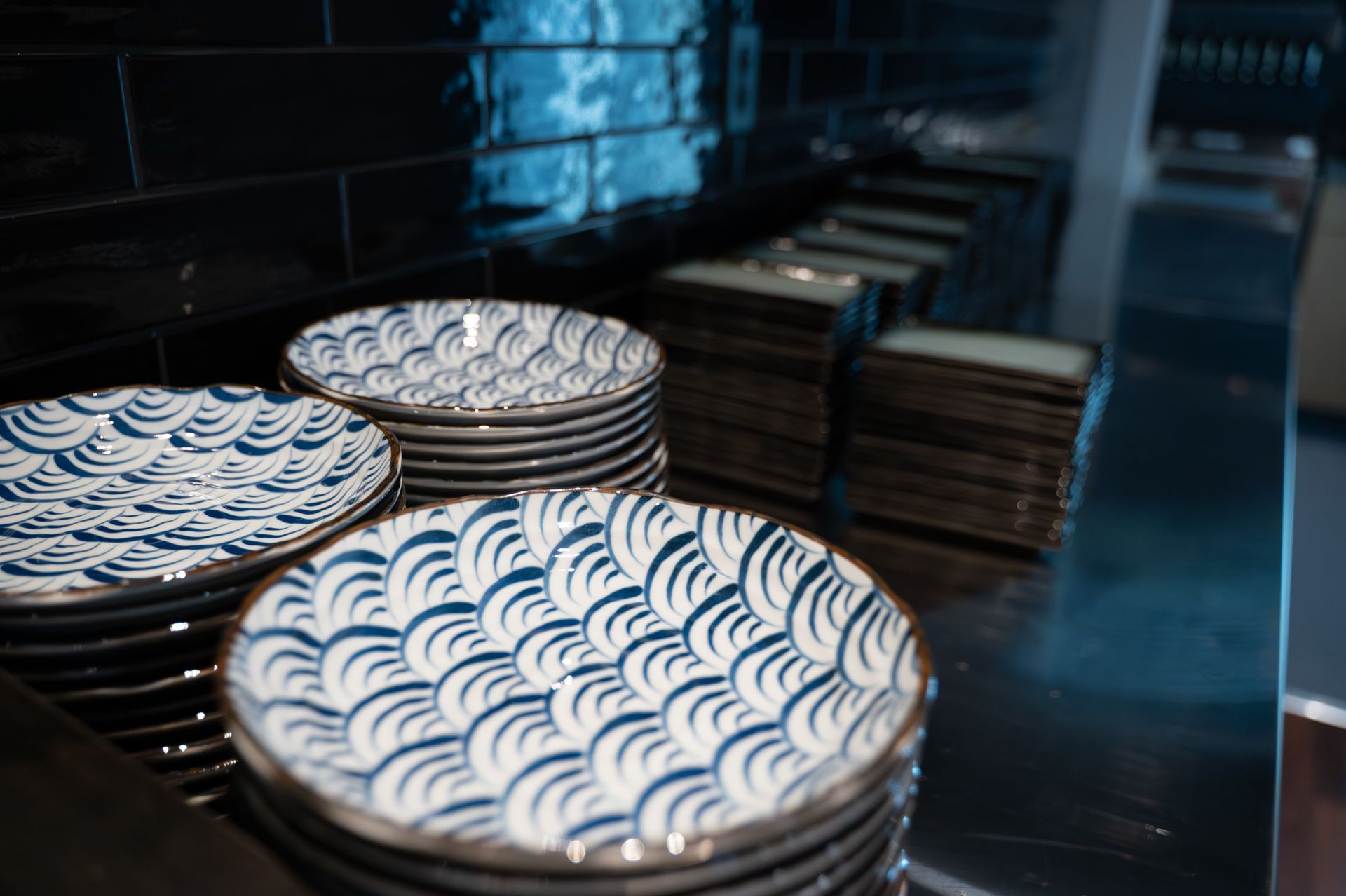 Stacks of blue-and-white patterned plates on a reflective metal shelf in a kitchen or bakery prep area