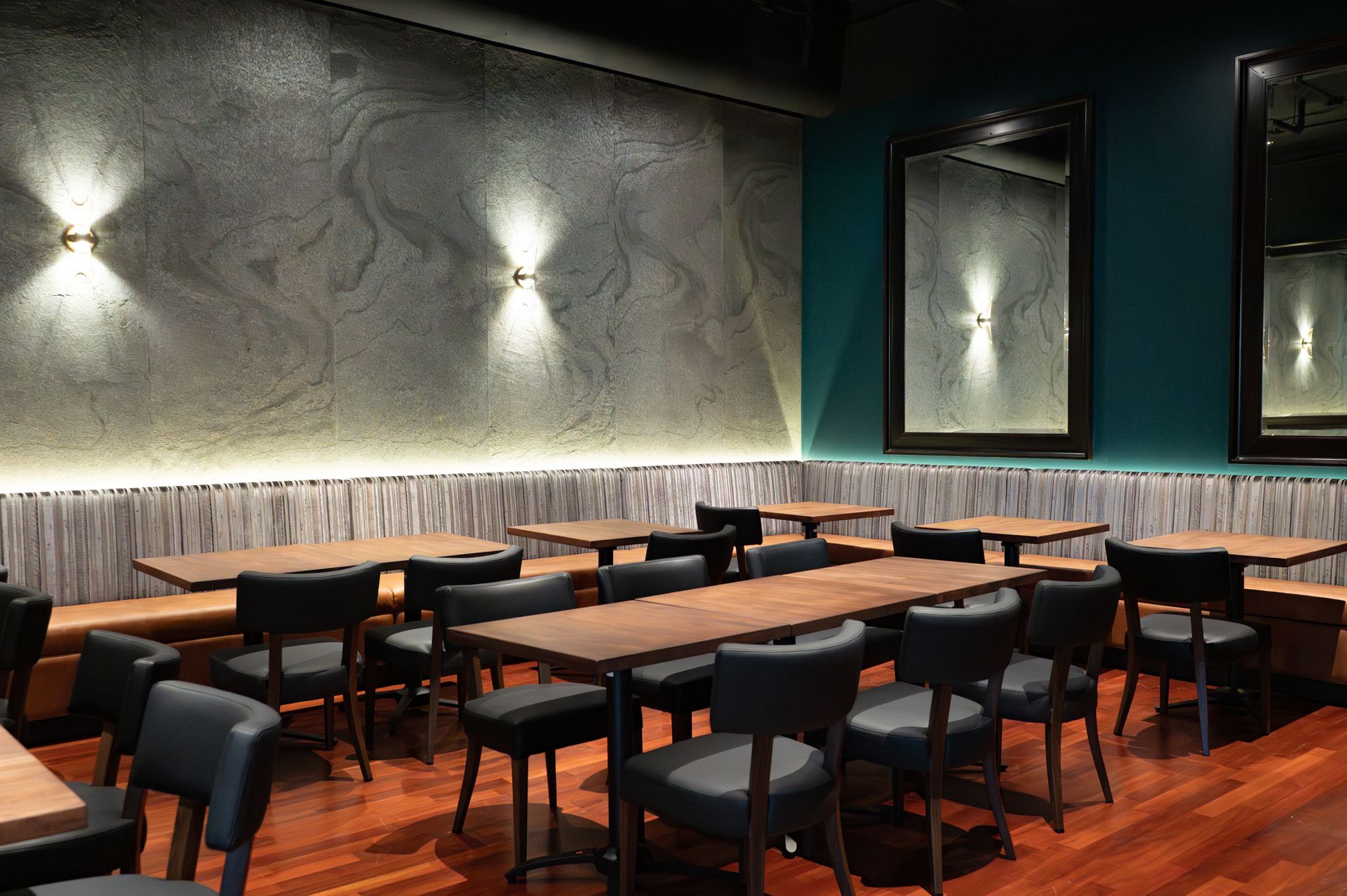 Modern empty restaurant interior with dark tables, black chairs, textured gray walls, and warm wood flooring