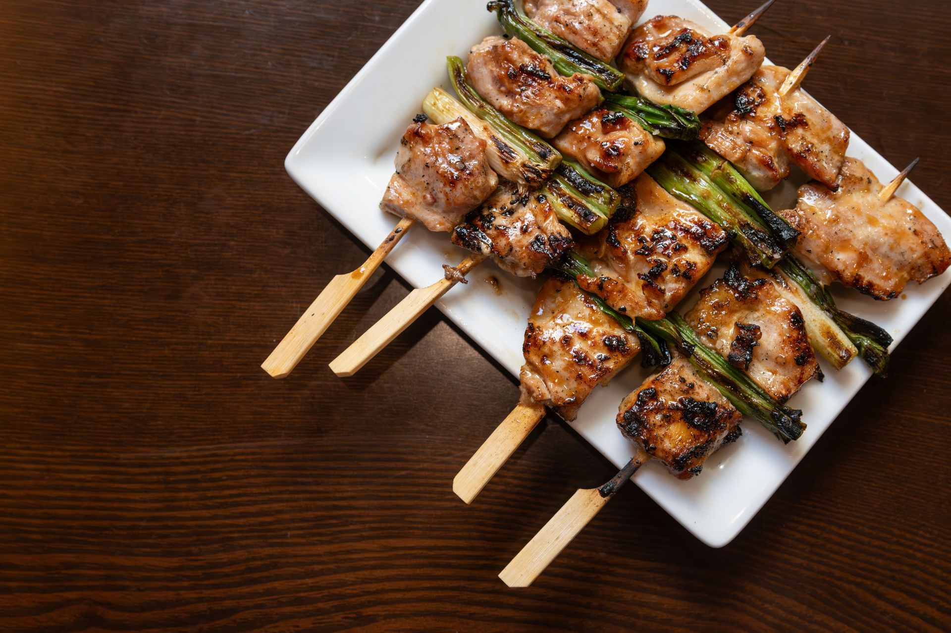 Grilled chicken skewers on a white plate over a dark wooden table