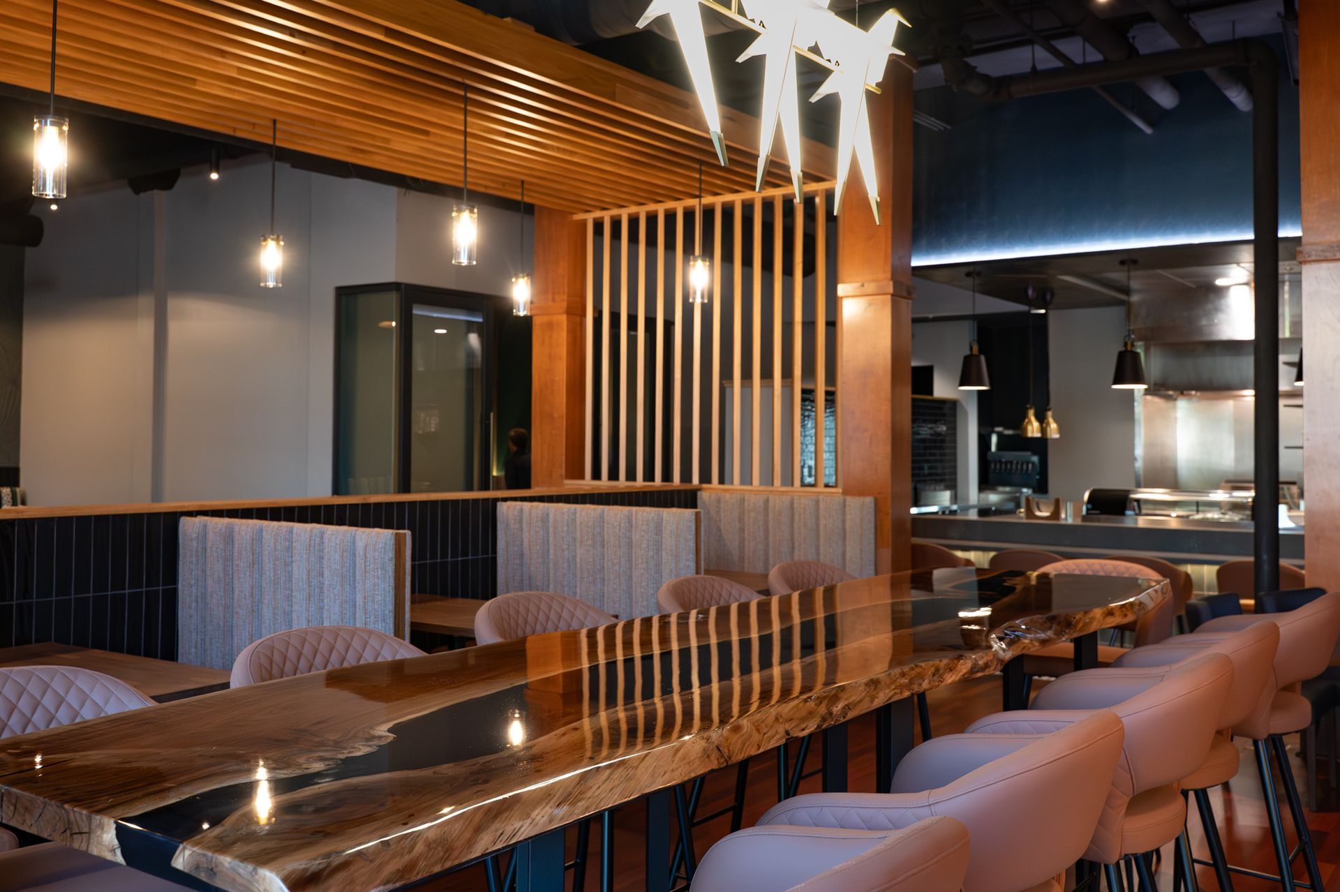 Modern restaurant interior with bar seating, wooden accents, pendant lights, and reflective tables.