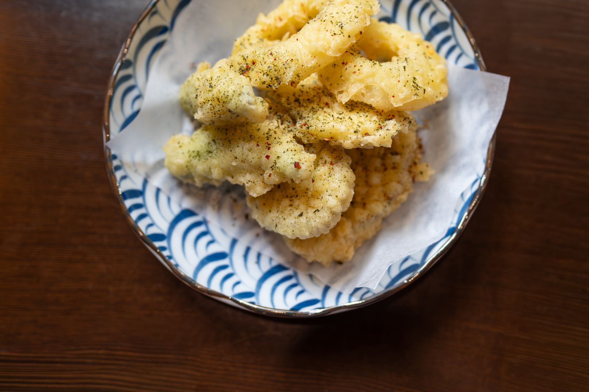 Bowl of pale yellow puffed snacks sprinkled with seasoning on a wooden table