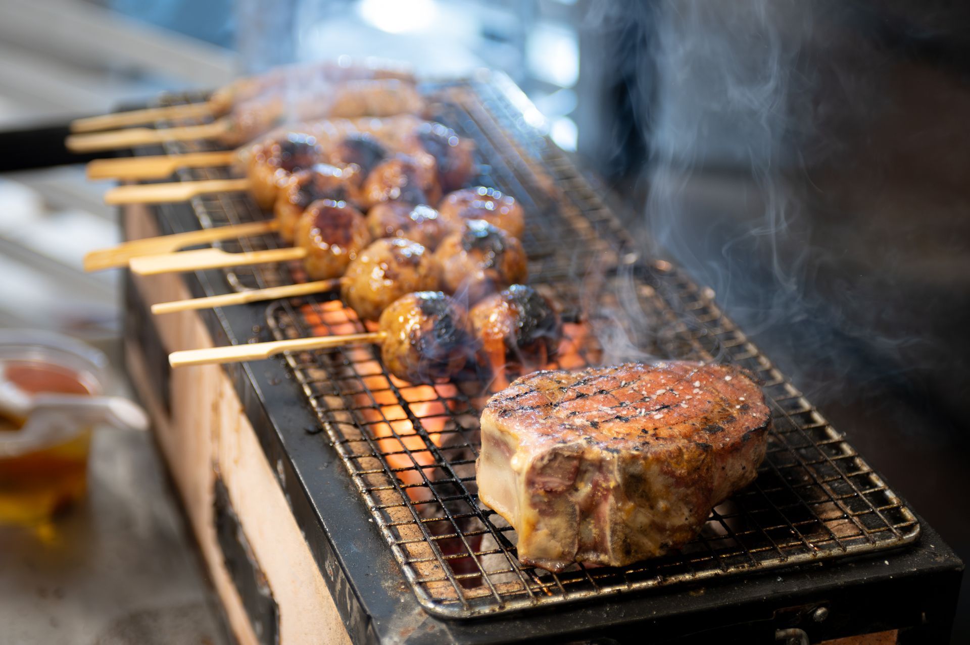 Meat skewers and steaks sizzling on a grill, with smoke rising from the hot coals.