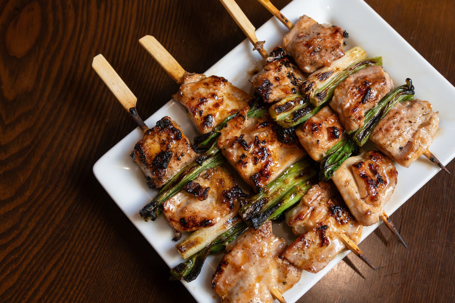 Grilled meat and green onion on skewers on a white platter on a gray table