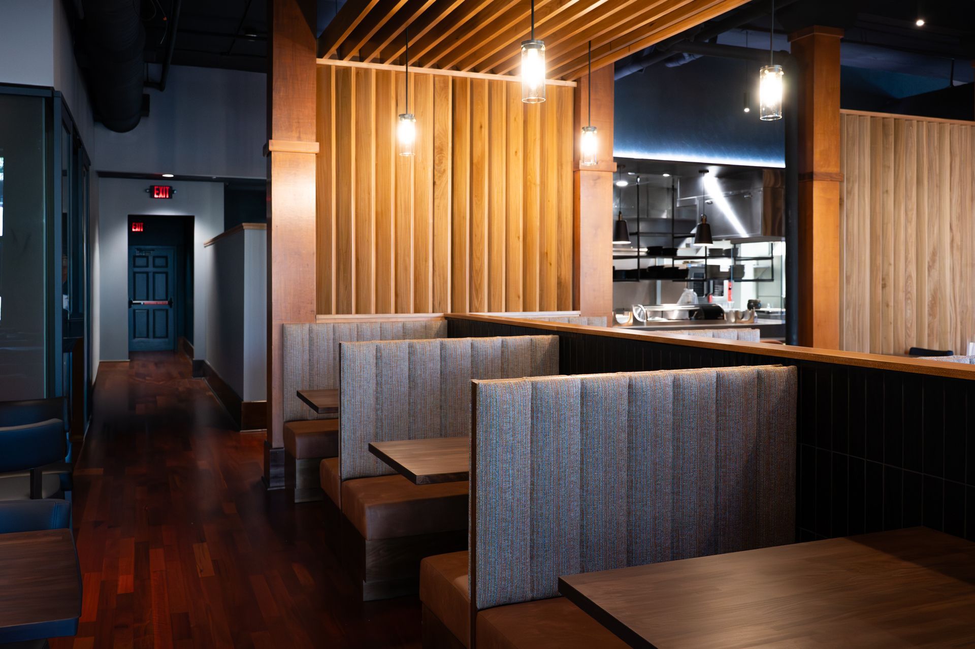 Modern restaurant interior with wooden booths, warm pendant lights, and dark polished floors